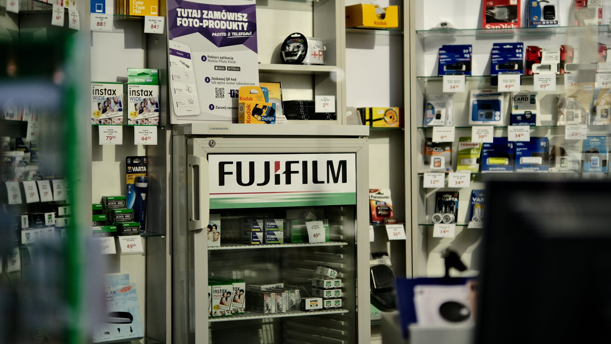 FUJIFILMの看板とフィルム商品が並ぶカメラ用品売り場の写真